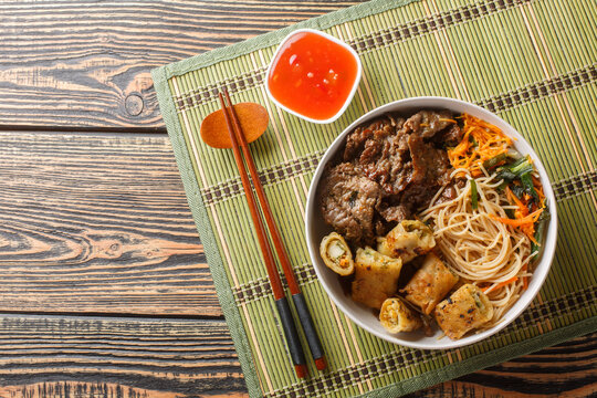 Vietnamese beef noodles salad bun bo xao is filled in fresh herb, savory beef, vegetables and fried spring rolls closeup on the table. Horizontal top view from above