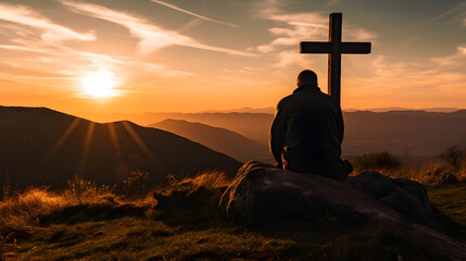 Silhouette of a man kneeling praying at the Cross of Jesus on a hill at sunrise