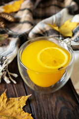 Autumn concept with drink, creative flat lay. Cup of hot sea ​​​​buckthorn tea with lemon, warm scarf and maple leaves on rustic background.