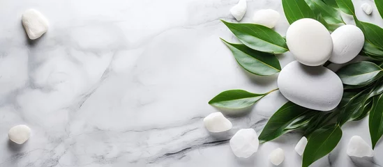 Fototapete Spa The background concept for a spa is depicted by the presence of white stones, a towel, and green plant leaves on a marble background, providing room for customization. This concept represents body