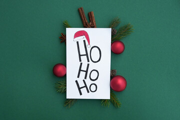 Congratulation  white postcard with inscription ho ho ho. Fir branch, decorations and Christmas spices on green background. Xmas or New Year greeting card template. Winter holiday theme. Flat lay.