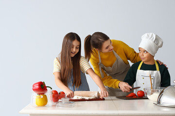 Female chef with little children during cooking class on light background