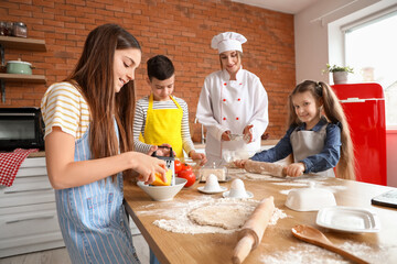 Female chef with group of little children preparing pizza during cooking class in kitchen