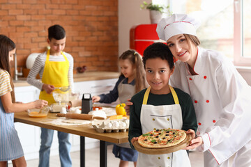 Female chef with little boy and prepared pizza after cooking class in kitchen