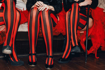 Crop photo of circus performers women sitting in dressing room, legs in striped red-black...