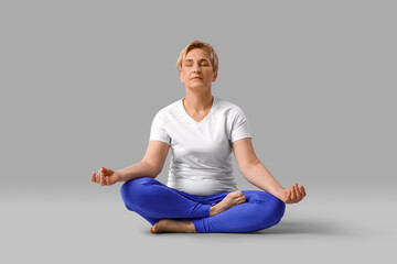 Sporty mature woman practicing yoga on light background