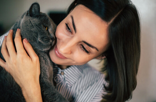 Pet like best friend. Close up photo of young cute woman at home holding and hugs her British shorthair cat in hands.