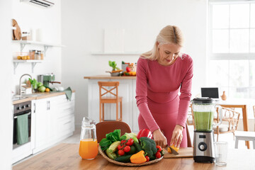 Sporty mature woman cutting lemon for healthy smoothie in kitchen