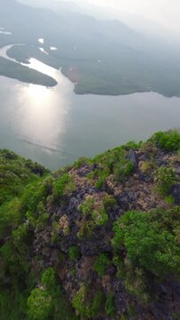 Vertical video. Aerial view dive from mountain peak covered greenery forest vegetation tropical island sea. FPV sport drone shot flying over rock ridge sunny exotic natural scenery cinematic paradise