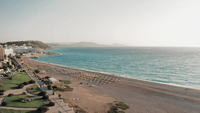 Aerial view of beautiful pebble beach with sunbeds and umbrellas at Aegean sea, drone footage. Rhodes, Greece. 
