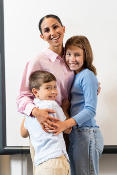 Overjoyed Kids Embracing Happy Multiethnic Female Teacher In Montessori School. Children Are Excited About The Start Of The School Year And The Lesson. Hug The Teacher During Breaks. Vertical Foto