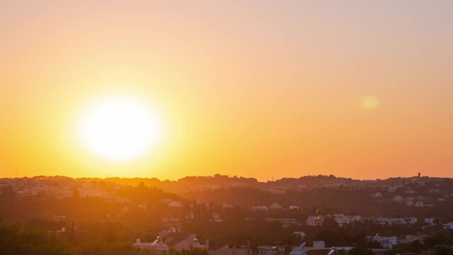Time-lapse summer evening, sunset over village on hilly area in Greece. Warm bright sun sets below horizon and dusk falls, lights turn on in small houses. Evening to night timelapse transition