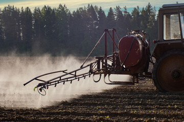 Spraying crops with chemicals such as pesticides or herbicides using sprayer mounted on wheeled tractor.