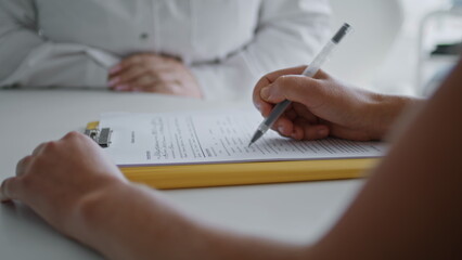 Unknown woman filling form for cosmetic procedures at desk clinic close up.