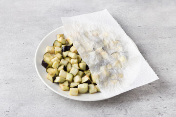 Drying of diced eggplants with a paper towel on a gray textured background. Processing eggplant before cooking, removing bitterness