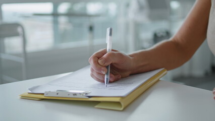 Woman hand writing papers on desk close up. Unknown woman with pen filling form.