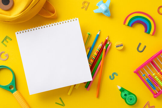School supplies and gear composition. Top view shot capturing empty notepad page with backpack and numerous educational materials on an isolated yellow surface. Suitable for text or advertisements