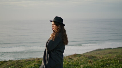 Woman standing cloudy seacoast in front gray ocean waves. Girl posing on shore. © stockbusters