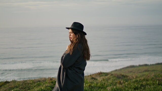 Woman standing cloudy seacoast in front gray ocean waves. Girl posing on shore.