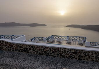 Sun loungers on terrace in the village of Imerovigli with amazing view of sunset over caldera in Santorini, Greece