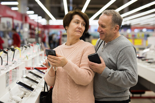 Senior couple choosing smartphone while shopping in tech store.