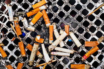close-up of a lot of cigarette butts in an ashtray outside. Flatlay. Cigarettes and smoking are...