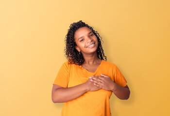 Black woman smiling with eyes closed and hands on her chest, having good and happy thoughts and feelings, against a yellow background. Mental health and yellow September concept.