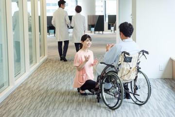 病院で車椅子に乗った患者と会話をする看護師