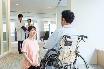 病院で車椅子に乗った患者と会話をする看護師