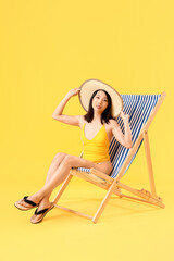 Beautiful Asian woman relaxing in deck chair on yellow background