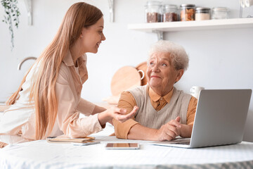 Senior woman with her granddaughter using laptop in kitchen
