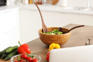Wooden bowl with fresh salad on table in kitchen, closeup