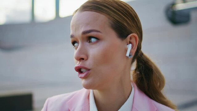 Woman wearing earbuds talking sitting urban area close up. Lady in earphones