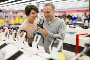 Fototapeta na wymiar Middle aged wife and husband picking new smartphone in electronic store.