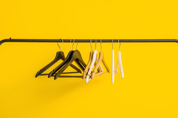 Rack with wooden clothes hangers on yellow background