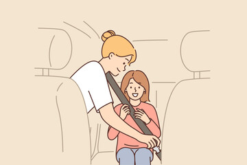 Caring mother uses child seatbelt to fasten little girl into passenger seat of car.