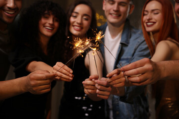 Happy friends with sparklers celebrating birthday indoors, focus on hands