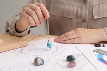 Astrologer using natal chart and pendulum for making forecast of fate at table, closeup. Fortune...
