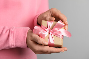 Woman holding gift box with pink bow on light grey background, closeup