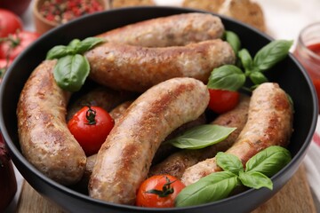 Bowl with tasty homemade sausages, basil leaves and tomatoes on table, closeup