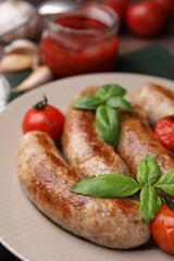 Plate with tasty homemade sausages, basil leaves and tomatoes, closeup