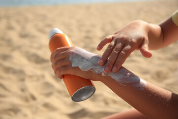 Child applying sunscreen on sandy beach, closeup. Sun protection care