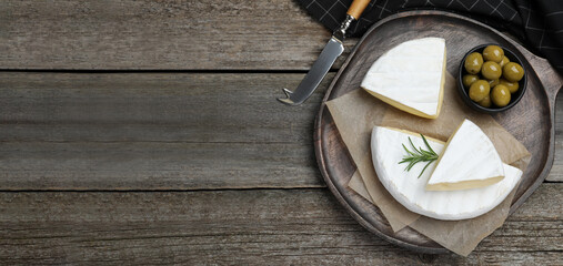 Tasty brie cheese and olives on wooden table, top view. Banner design with space for text