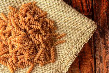 Raw whole grain fusilli pasta on rustic fabric over wooden table.