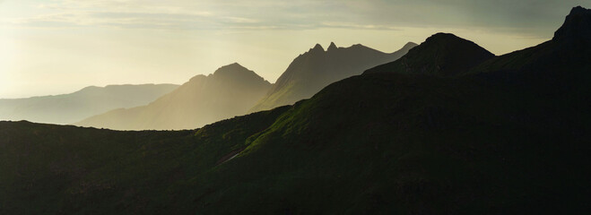 Panorama of abstract norwegian landscape at sunset, Smaltinden, Luröy, Helgeland, Nordnorge. Post summer storm dusk with mountain silhouettes. Green details in dark mountains scandinavia. Sommarnatt