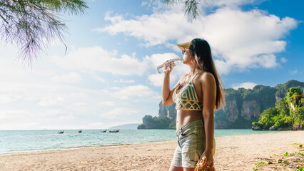 Traveler woman on vacation beach drinking water from bottle at sunny day Railay Beach Krabi, Summer lifestyle tourist girl travel Phuket Thailand holiday trip, Tourism beautiful destination place Asia