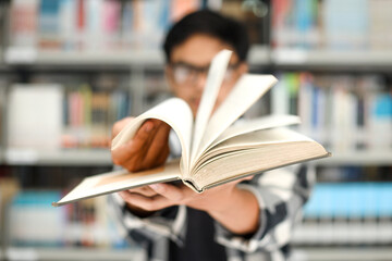 Close-up of hand flipping the book against blurry bookshelves background. 