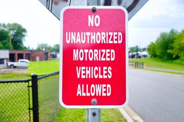 Close up of red no unauthorized motorized vehicles allowed sign against blurred street.