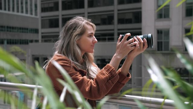 Young blonde woman taking photography modern city buildings.Photographer lady using camera for photoshoot.Photoshoot education.Attractive lady holding mirrorless photo camera looking on screen.