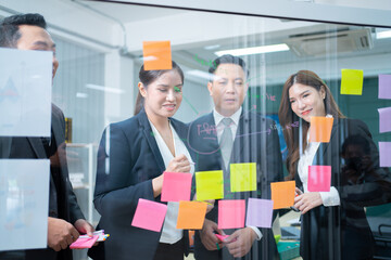 executives business asian entrepreneur of small company putting a adhesive note on glass in office during team meeting formulating business strategies.